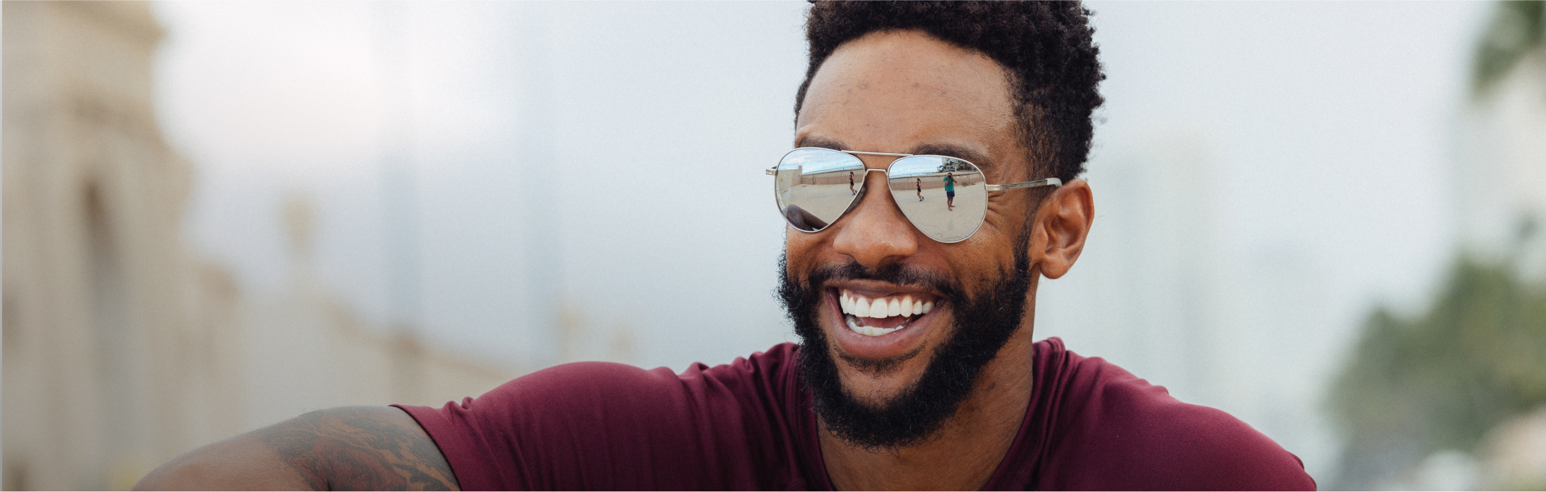 Man laughing wearing ROKA sunglasses with beachy reflection on lenses.
