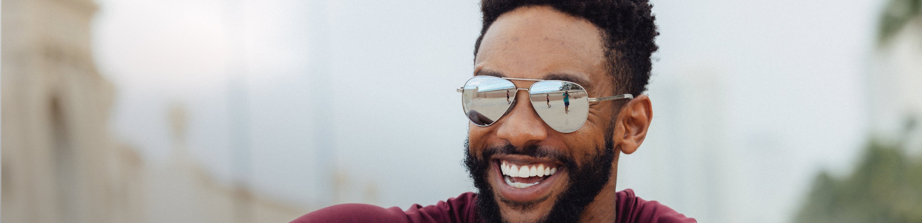Man laughing wearing ROKA sunglasses with beachy reflection on lenses.
