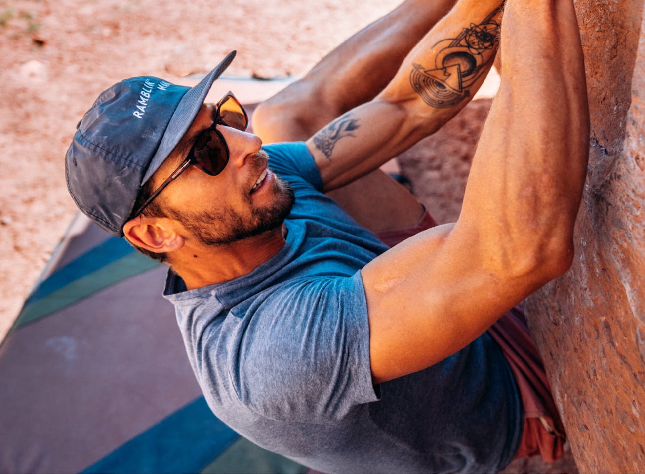 Man bouldering in desert wearing a hat and Rory sunglasses