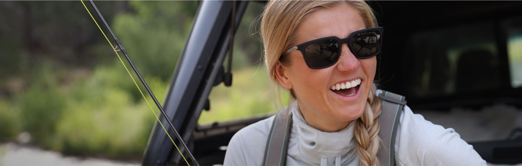 Woman with fishing rod laughing wearing ROKA sunglasses