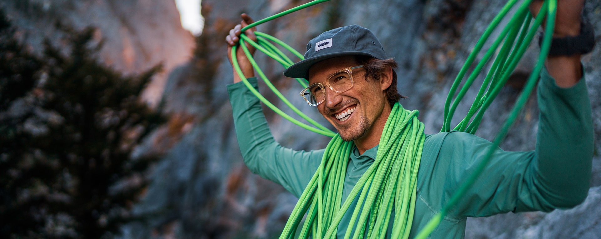 Man holding green climbing rope smiling and wearing ROKA eyeglasses