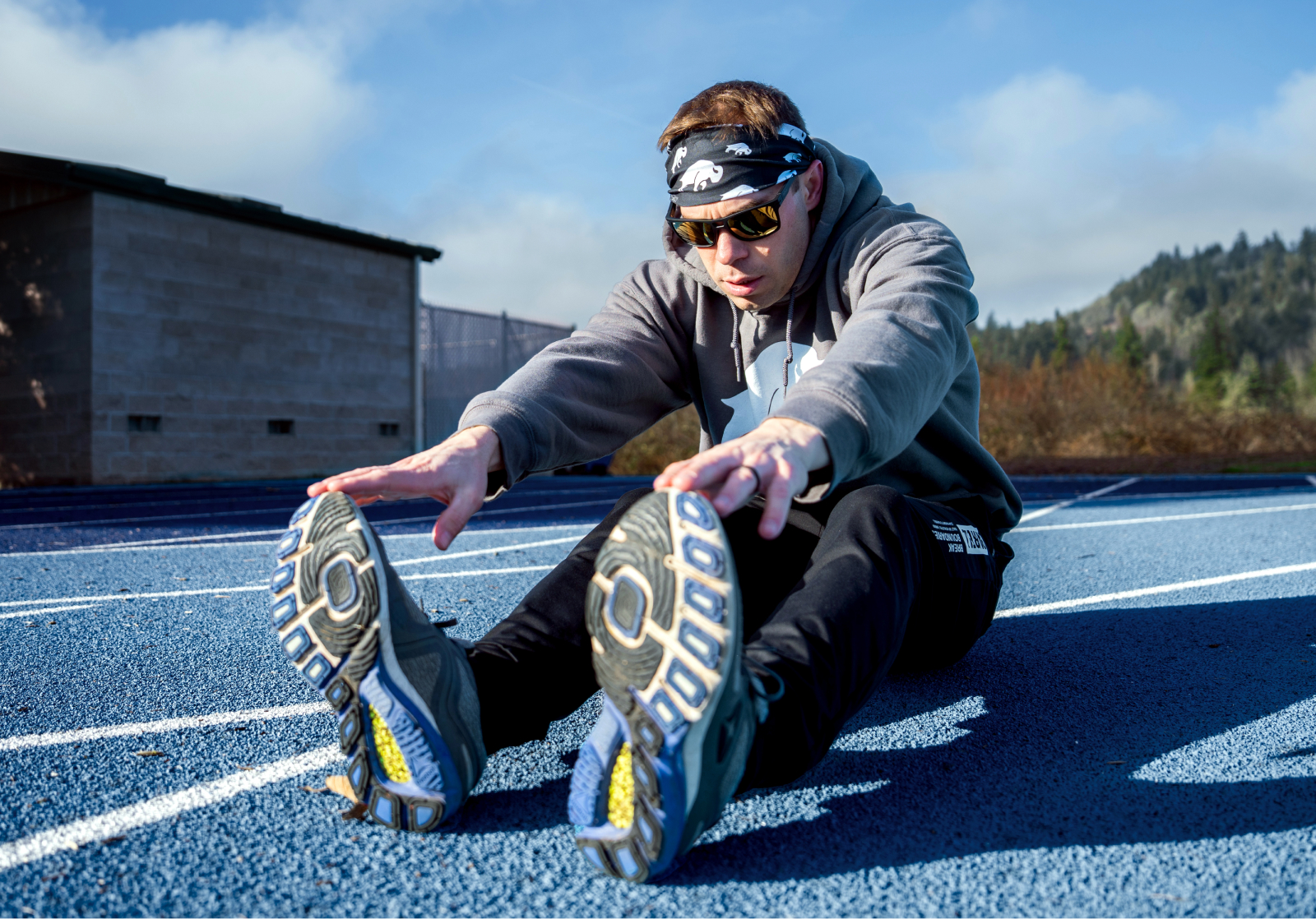 Man stretching on track wearing Kona sunglasses