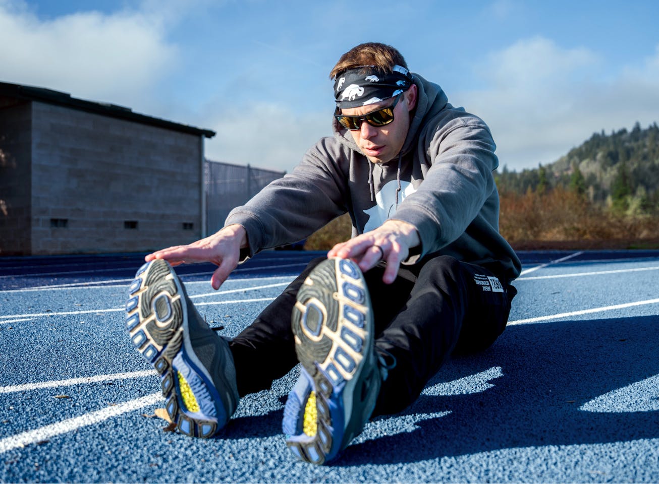 Man stretching on track wearing Kona sunglasses