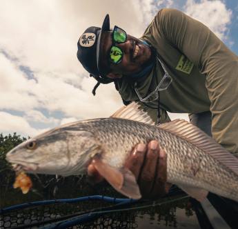 Man wearing green mirrored sunglasses and holding a fish