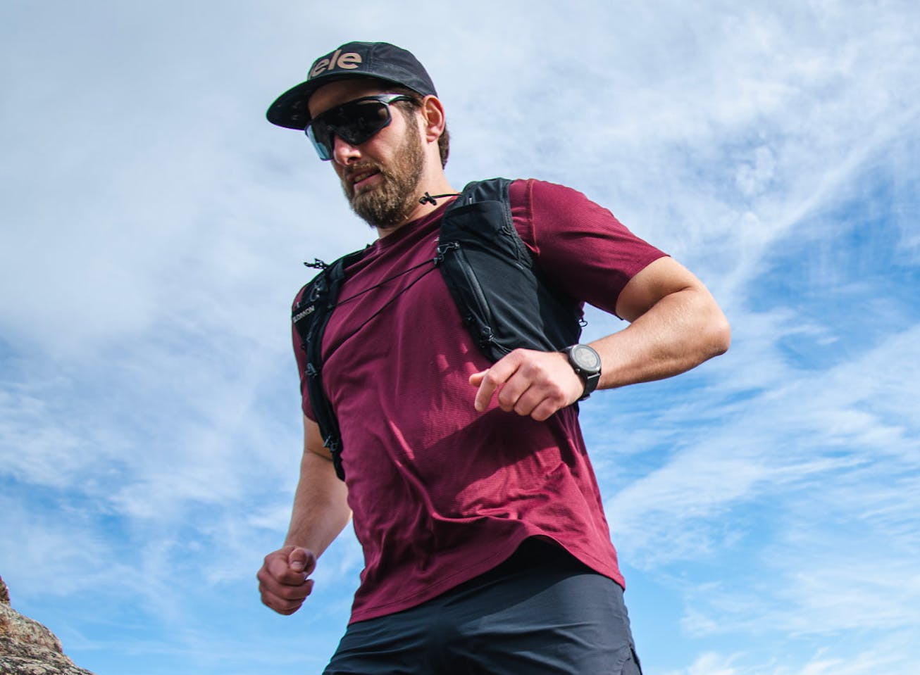 Man trail running wearing backpack and maroon shirt