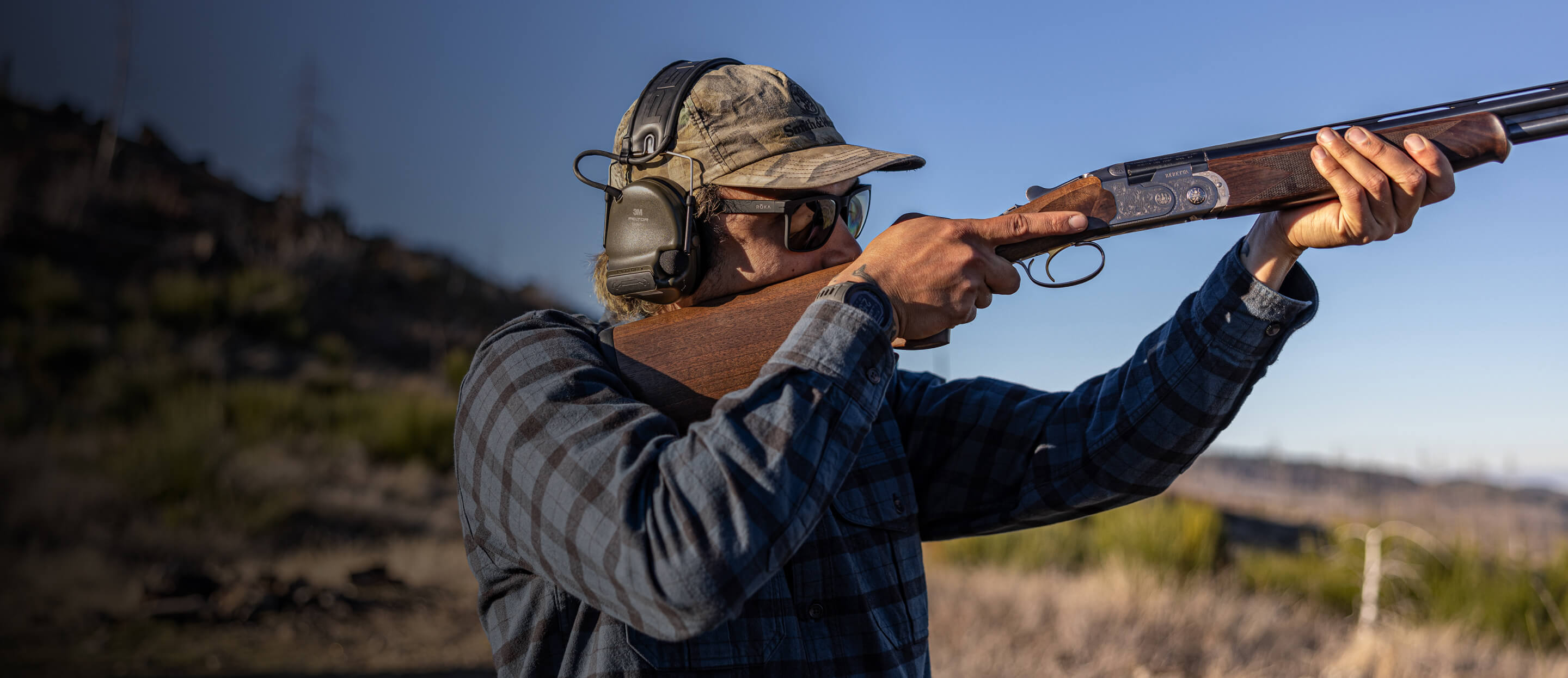 Man shooting rifle in camo hat and Barton sunglasses