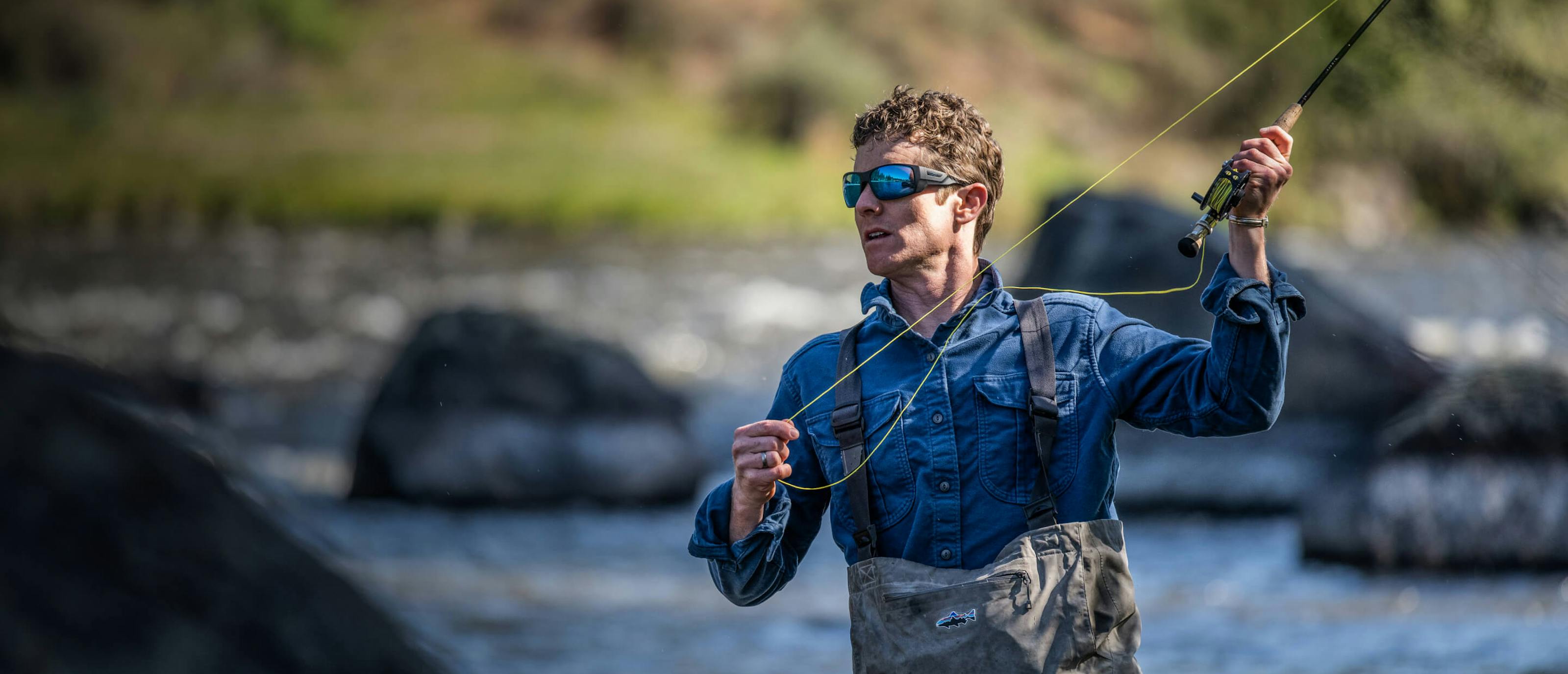 Man casting fishing rod wading in river