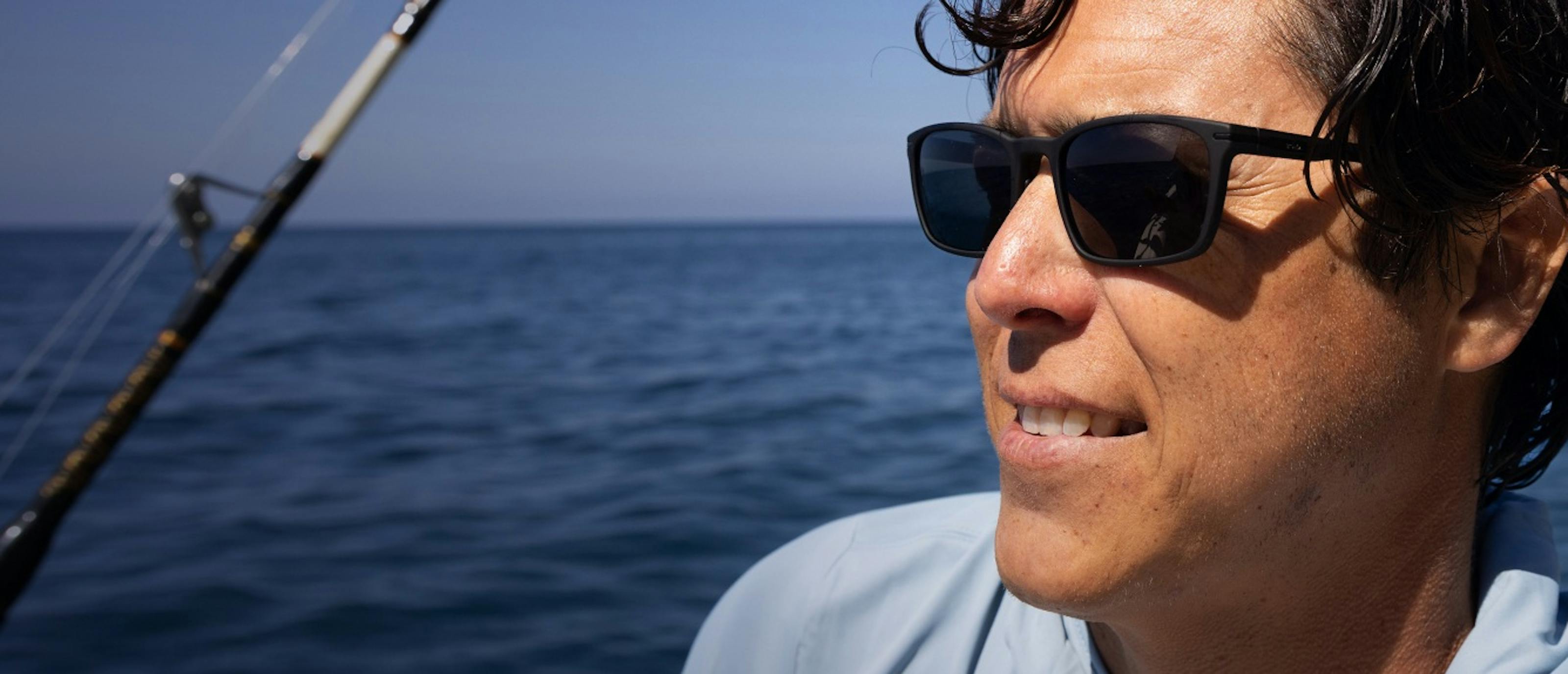 Man with fishing rod near ocean in Palmer sunglasses