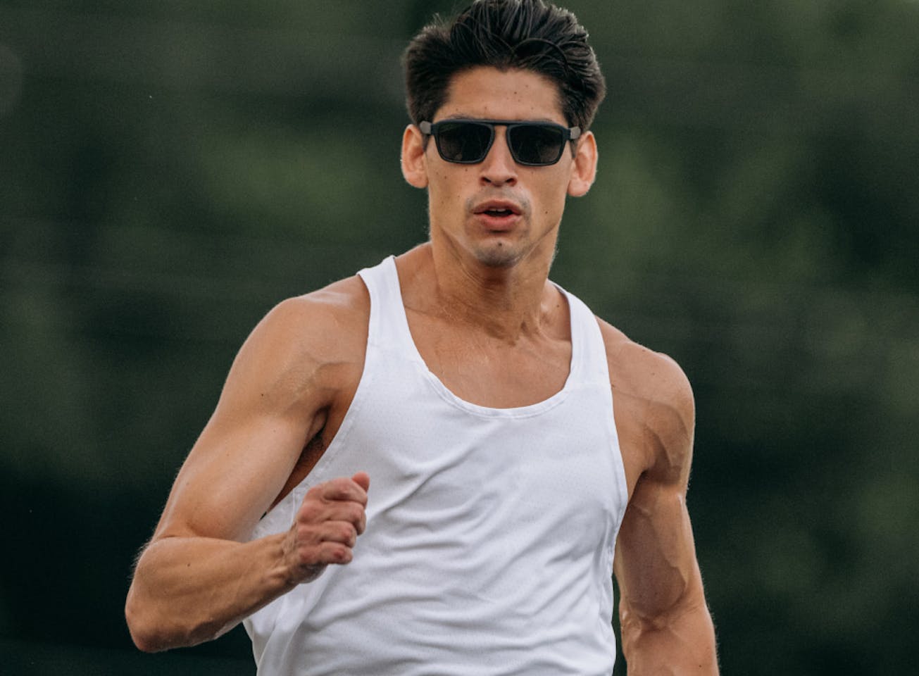 Man in white tank top running in Estacado sunglasses.