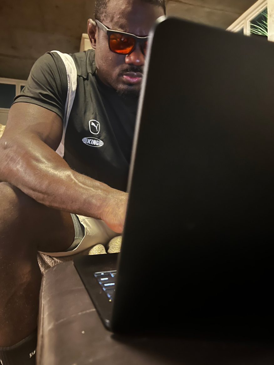 Man at coffee table on laptop wearing Red Lens glasses
