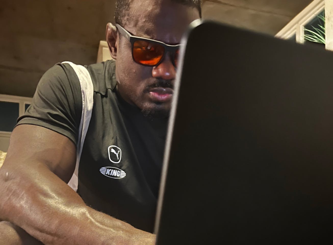 Man at coffee table on laptop wearing Red Lens glasses