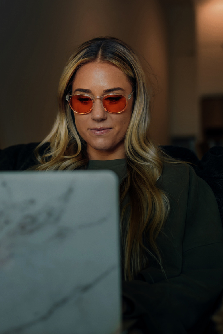Blonde haired woman on laptop wearing Red Lens glasses