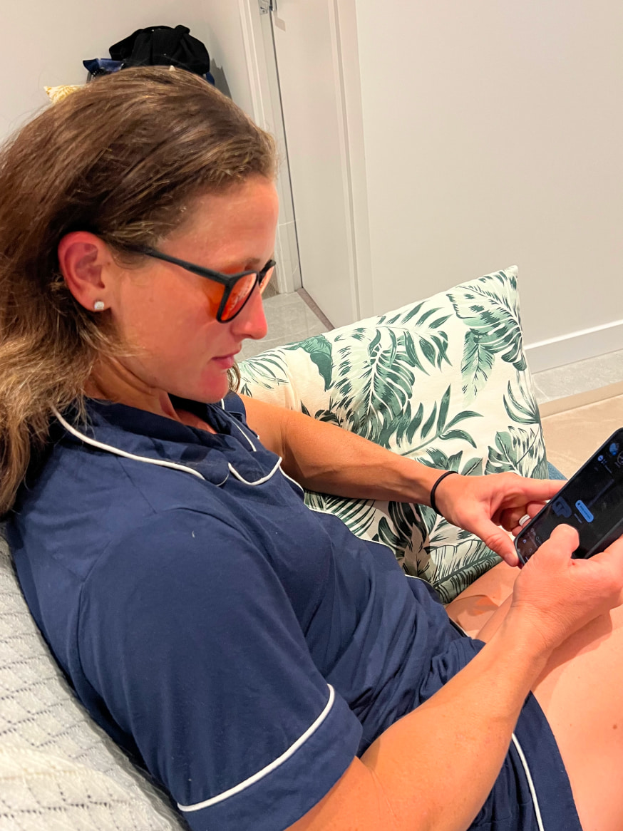 Woman on couch looking at phone wearing Red Lens glasses