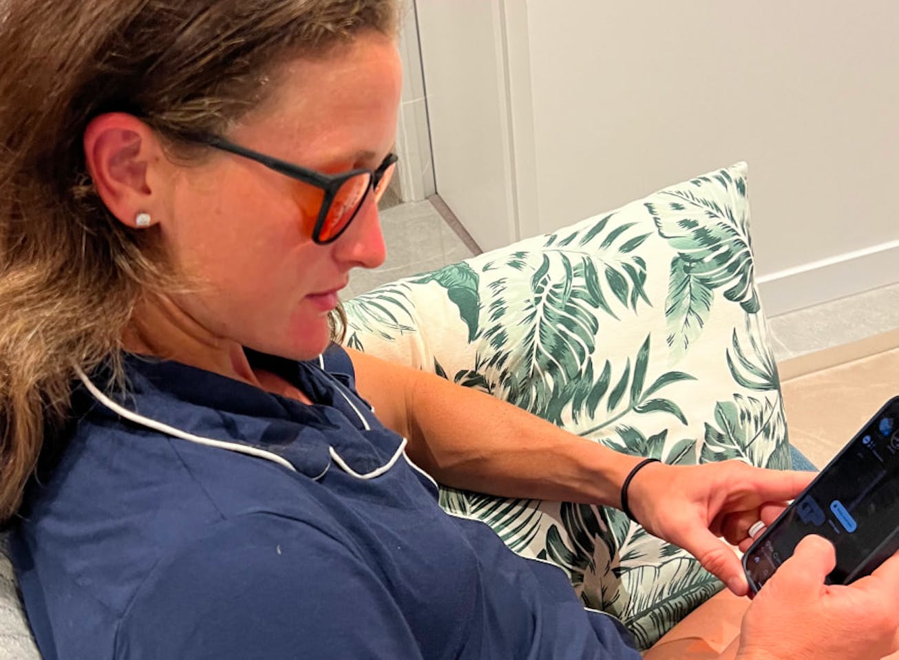 Woman on couch looking at phone wearing Red Lens glasses
