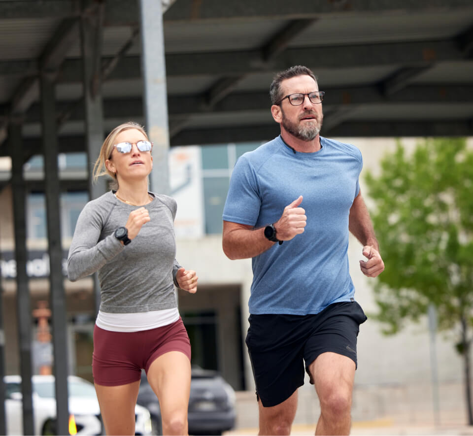 Man and woman running under bridge wearing ROKA glasses