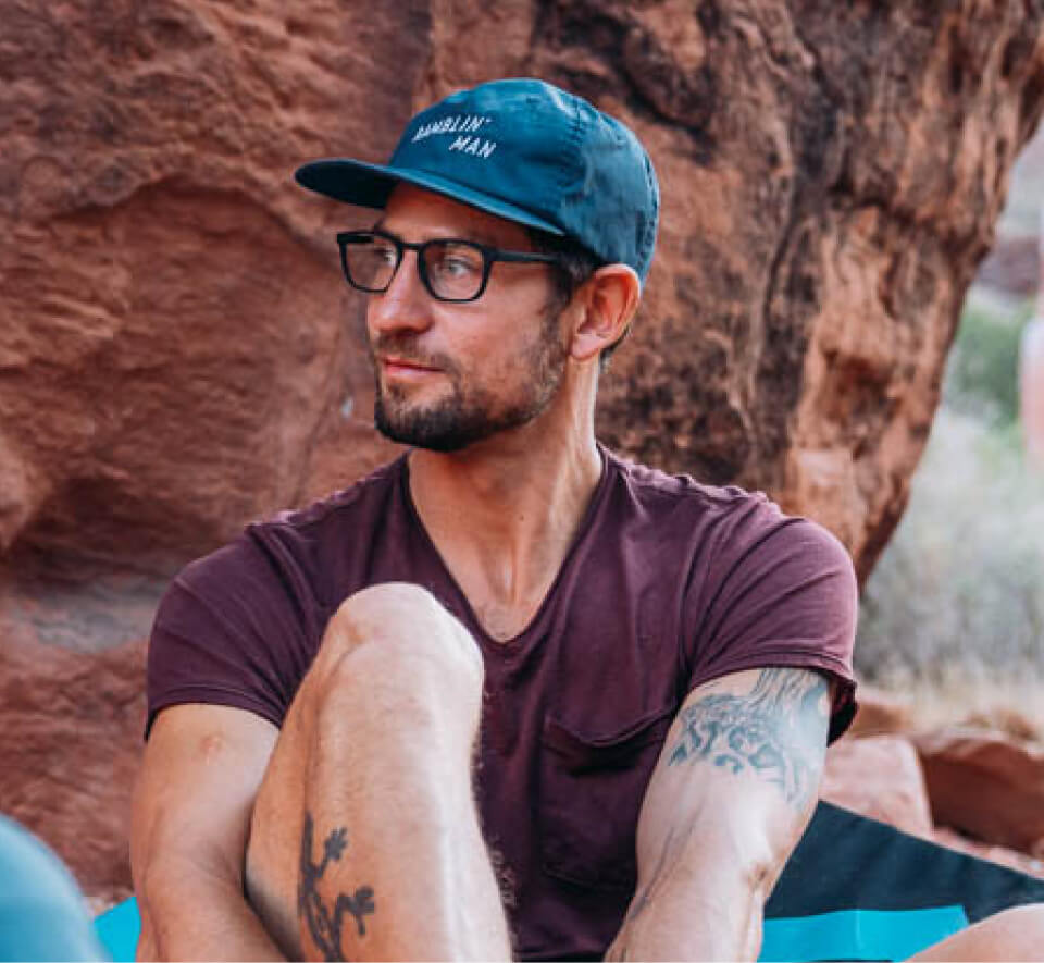 Man putting on climbing shoes in boulder area wearing ROKA glasses