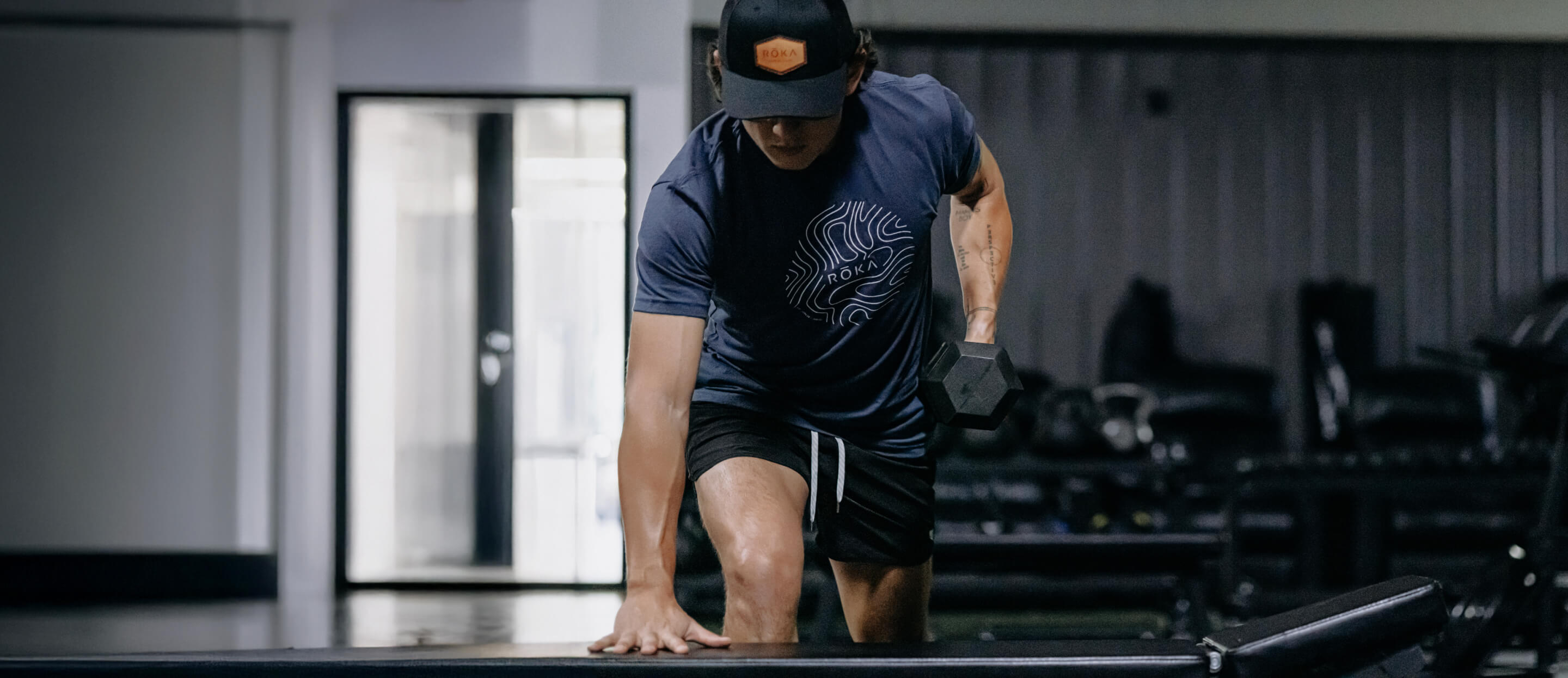 Man doing dumbess rows in ROKA topo t-shirt