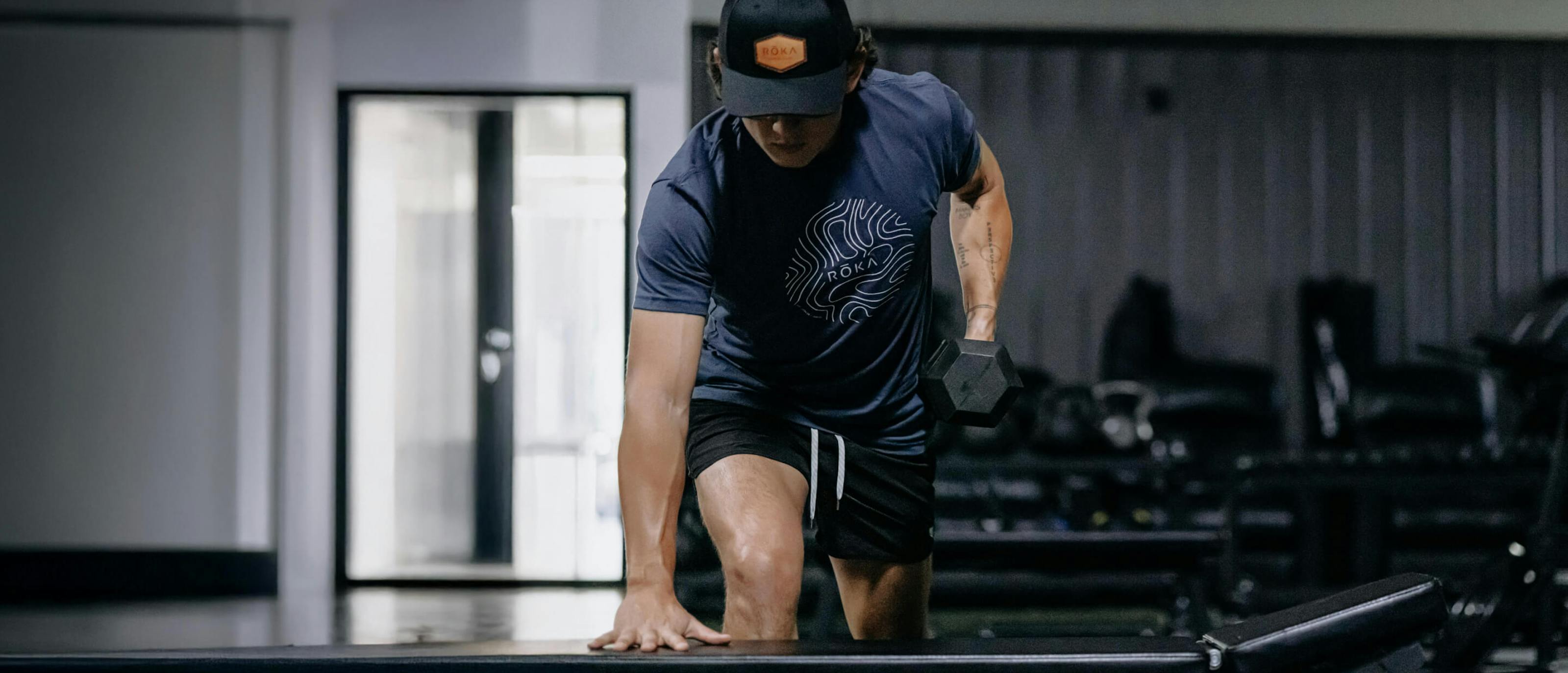 Man doing dumbess rows in ROKA topo t-shirt