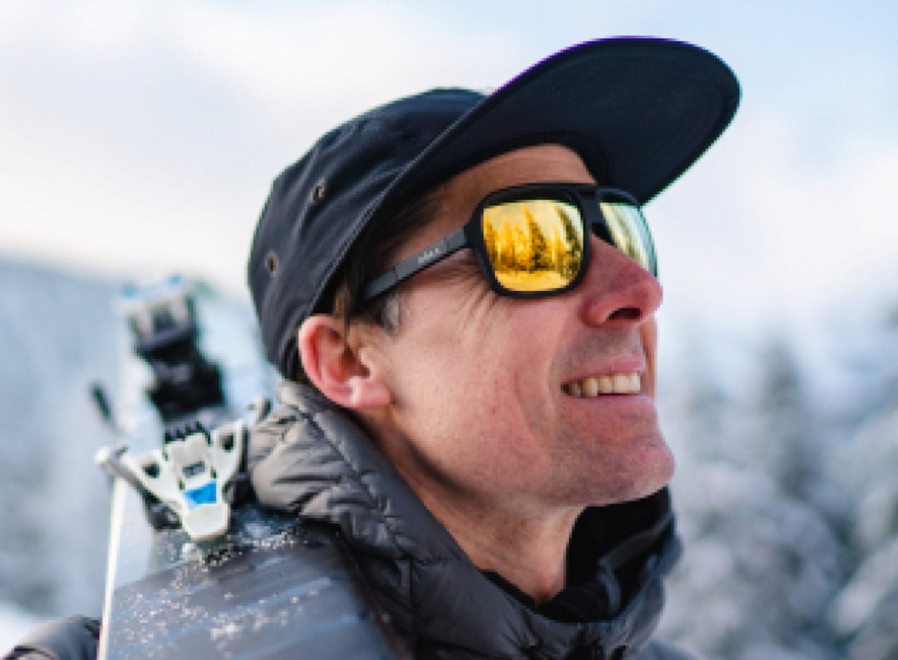 Man in snow carrying skis wearing Torino sunglasses