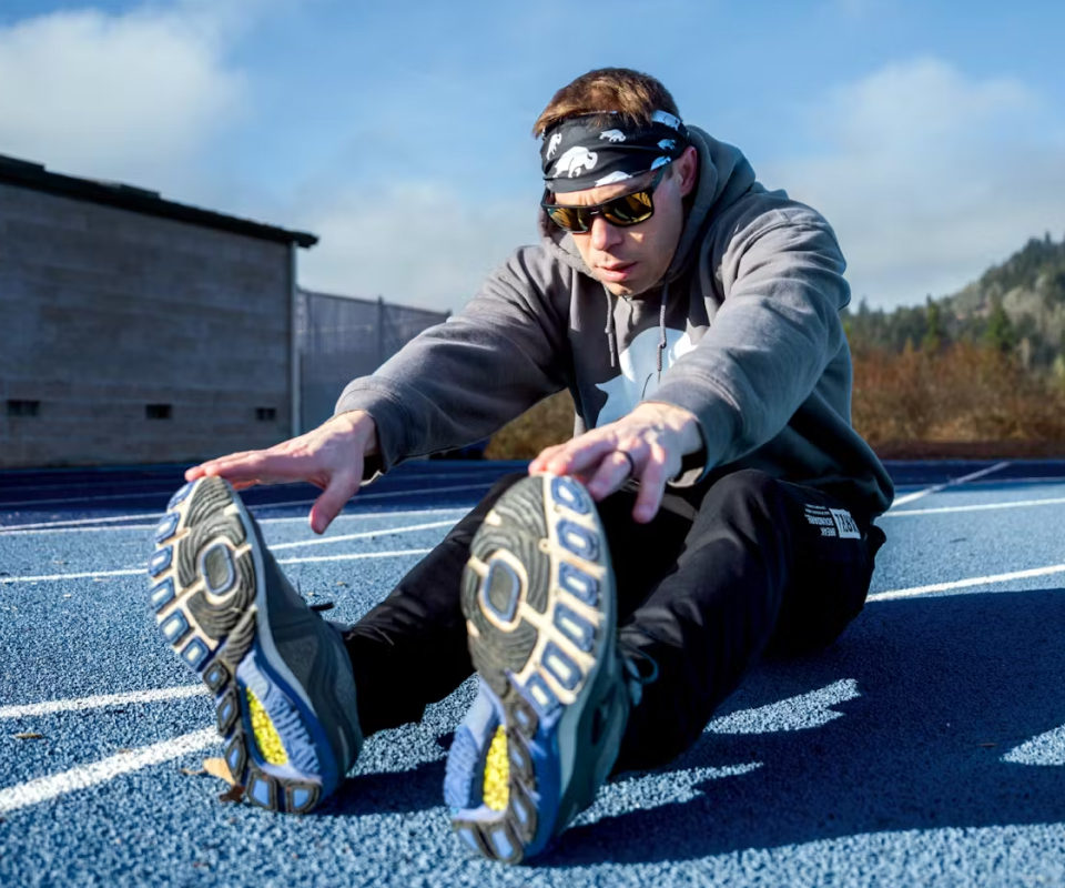 Man stretching on track wearing headband and ROKA Sunglasses