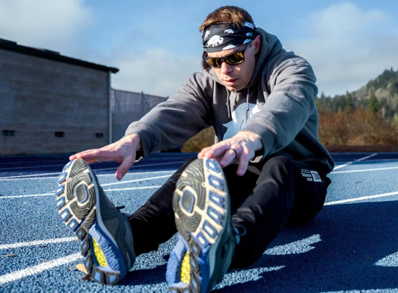 Man stretching on track wearing headband and ROKA Sunglasses