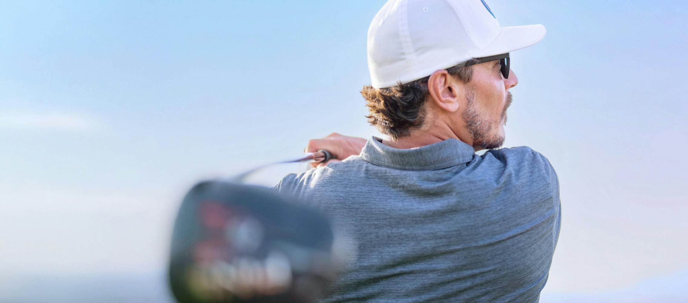 Man in white hat swinging golf club