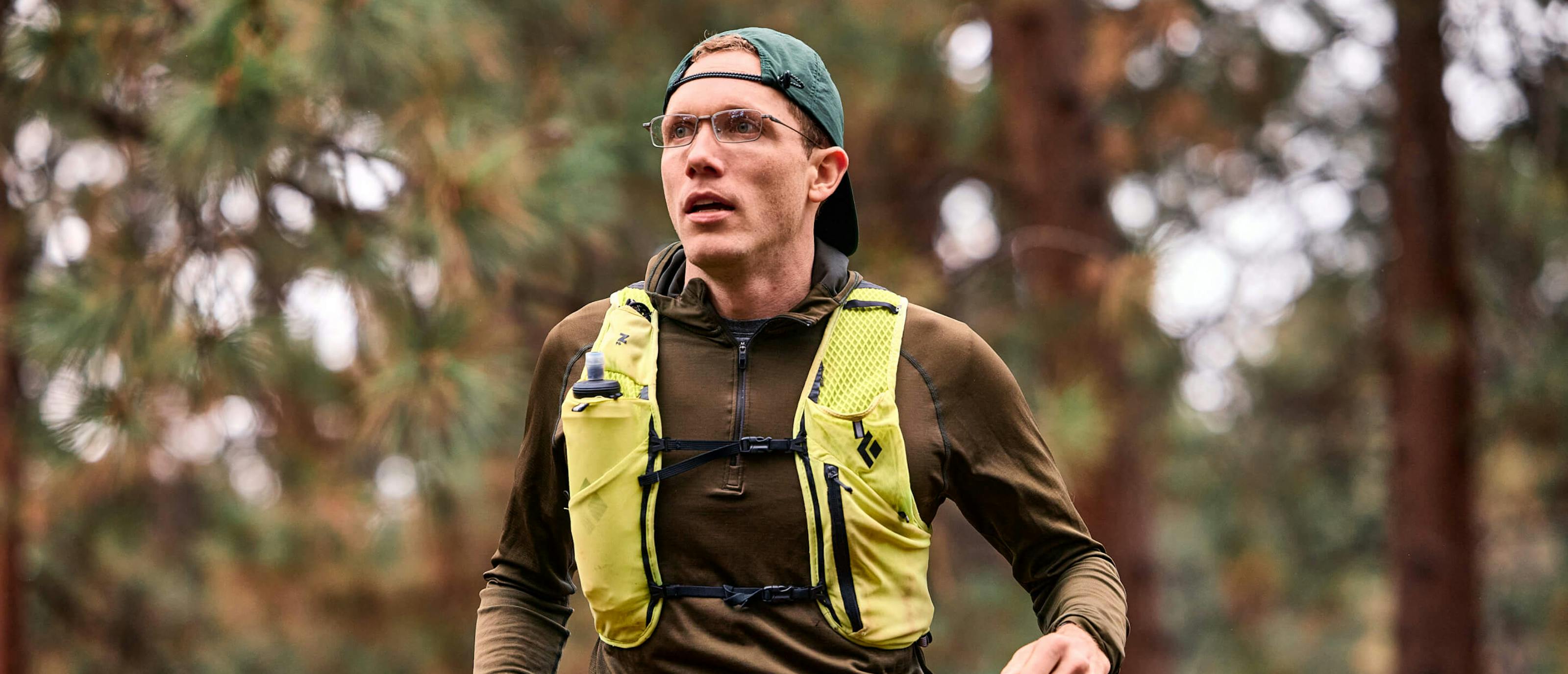 Man wearing ion glasses and green jacket in woods