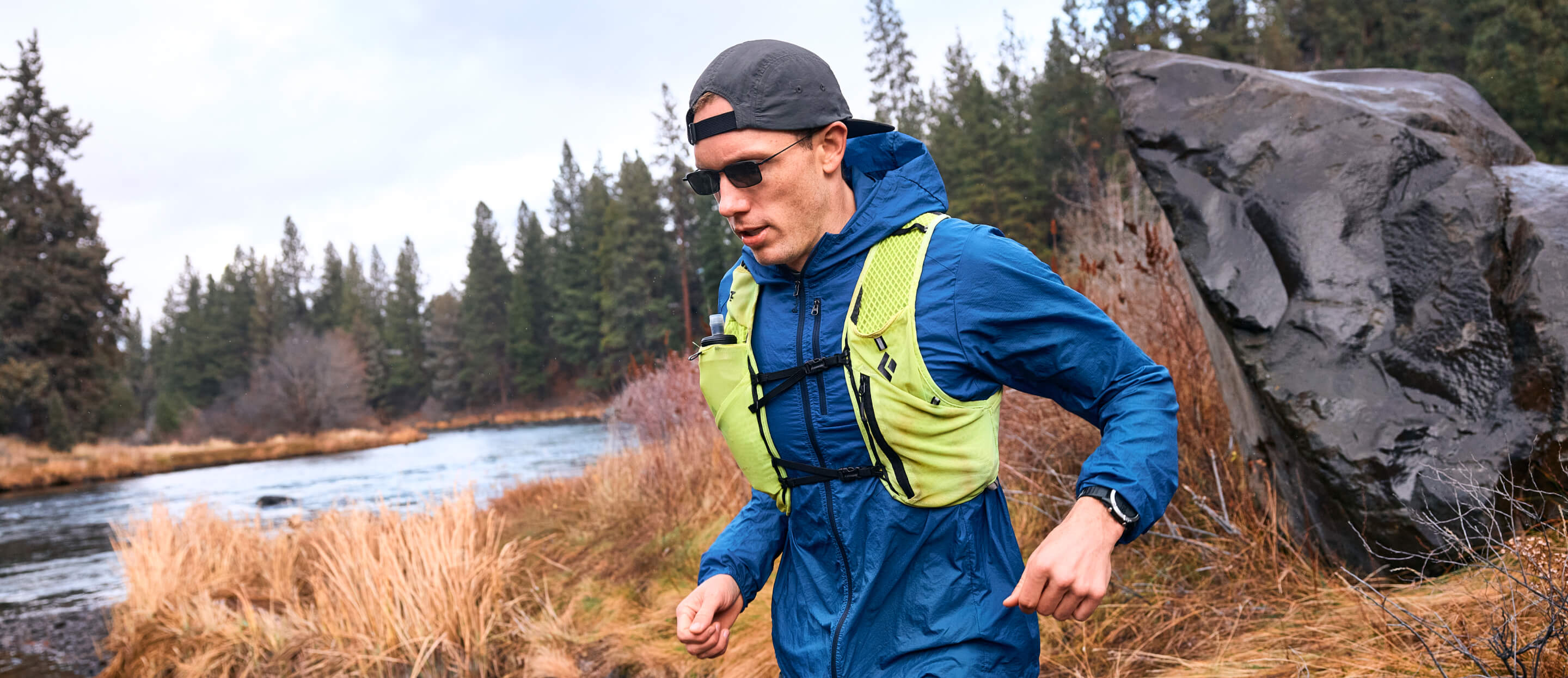 Man running near creek wearing blue jacket and backwards hat