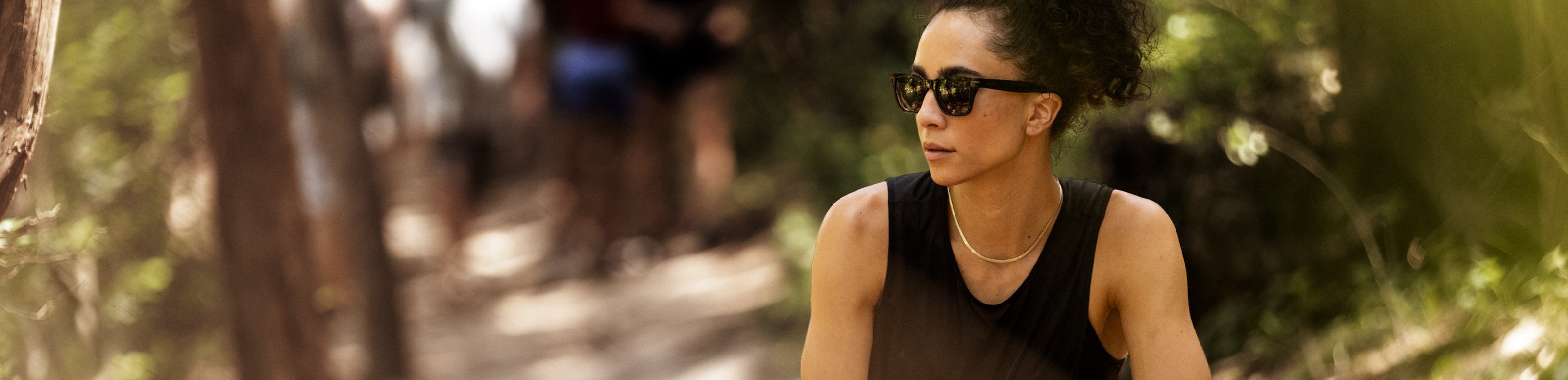 Woman stretching in woods wearing ROKA sunglasses and black tank top