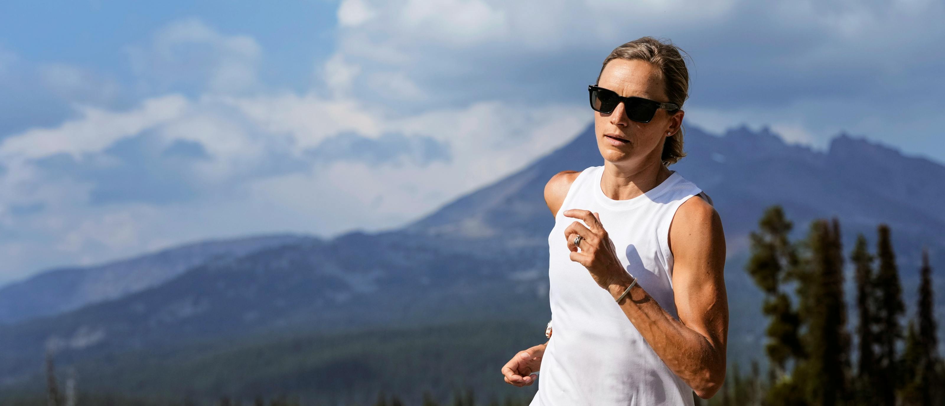 Woman jogging in white tank top in front of mountain