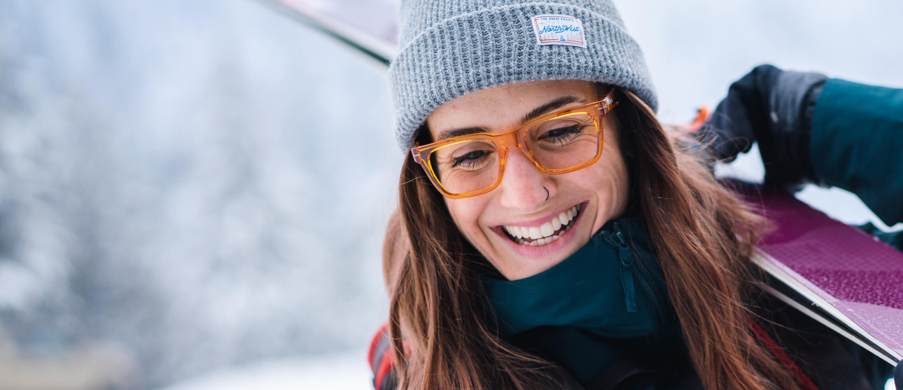 Woman smiling carrying skis wearing Lockhart orange eyeglasses