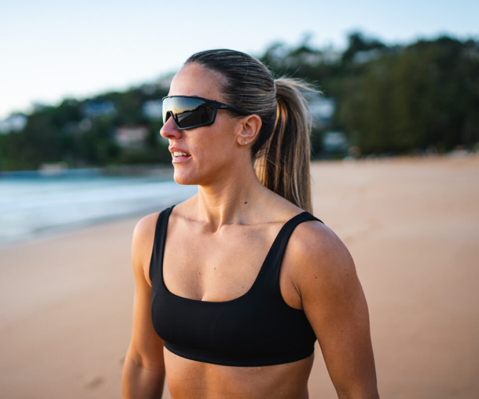 Woman on beach wearing black tank top and ROKA sunglasses