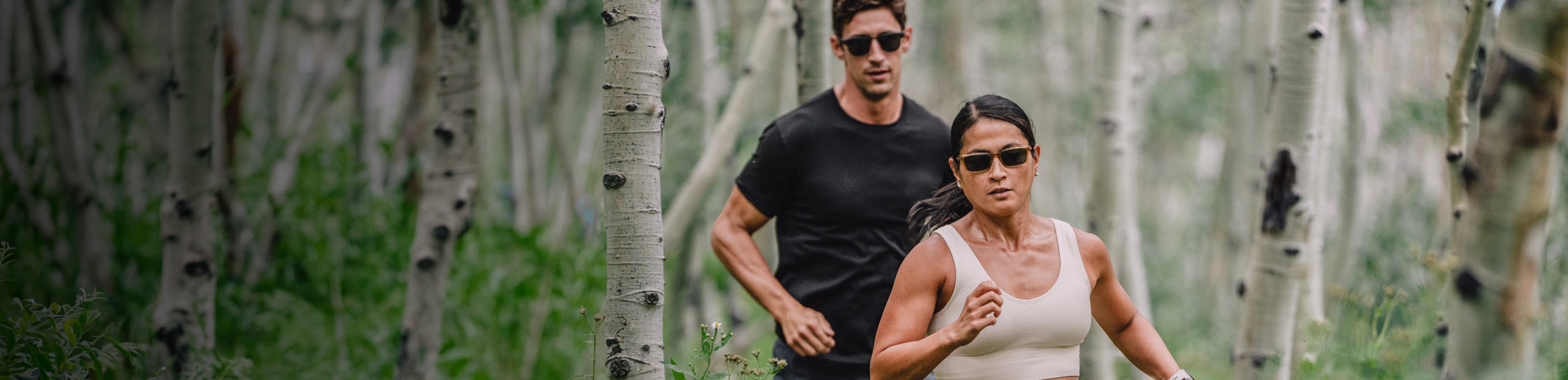 Man and woman running in the woods wearing ROKA sunglasses