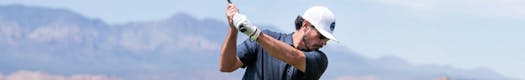 Man swinging golf club on desert golf course