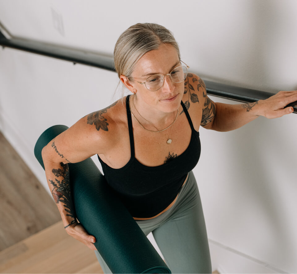 Woman carrying yoga mat in black top and Alto Eyeglasses