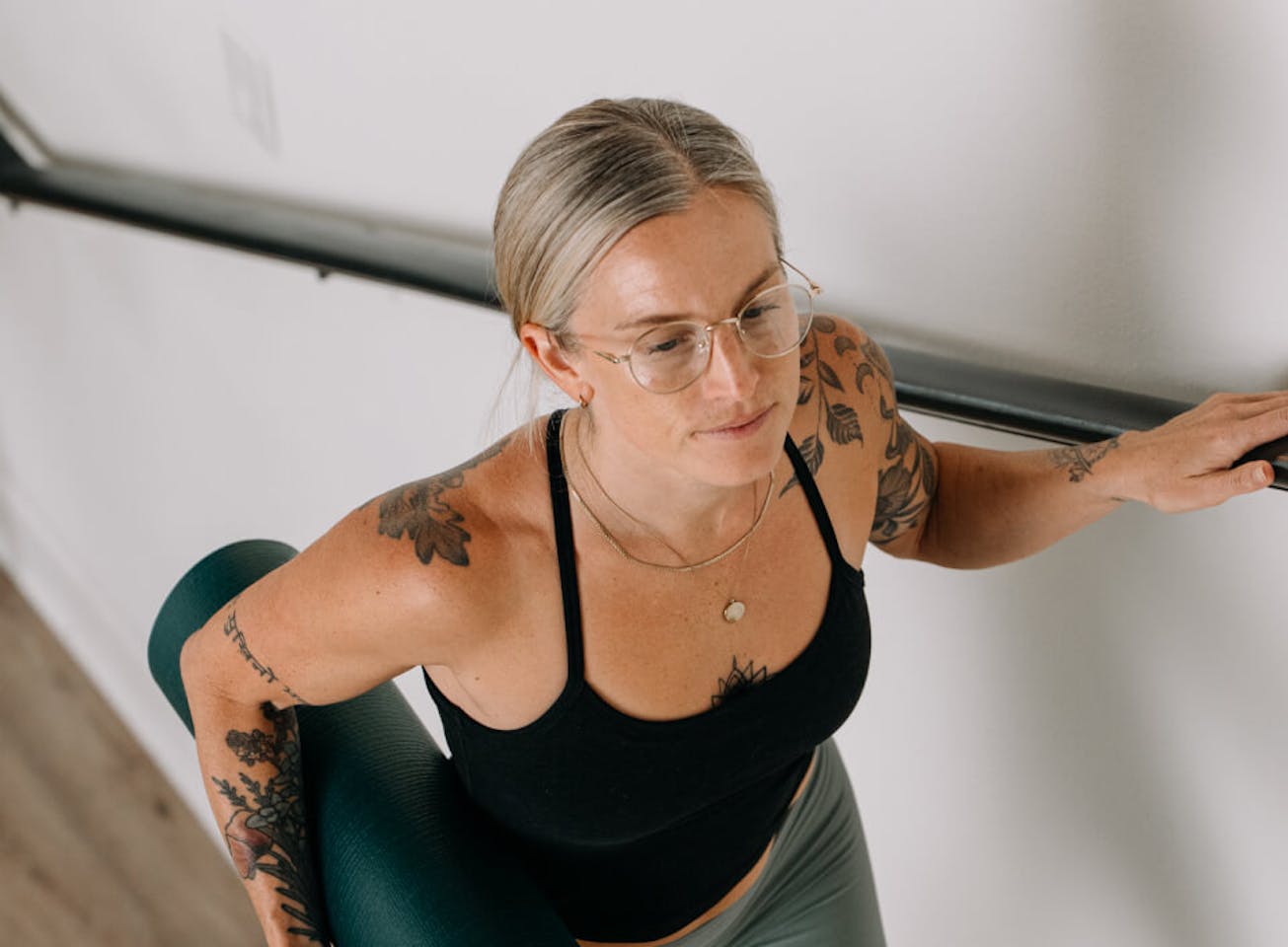 Woman carrying yoga mat in black top and Alto Eyeglasses