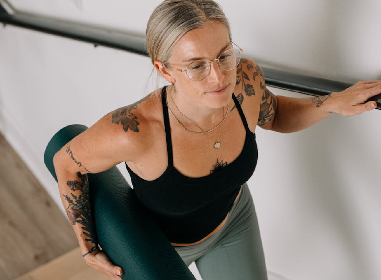 Woman carrying yoga mat in black top and Alto Eyeglasses